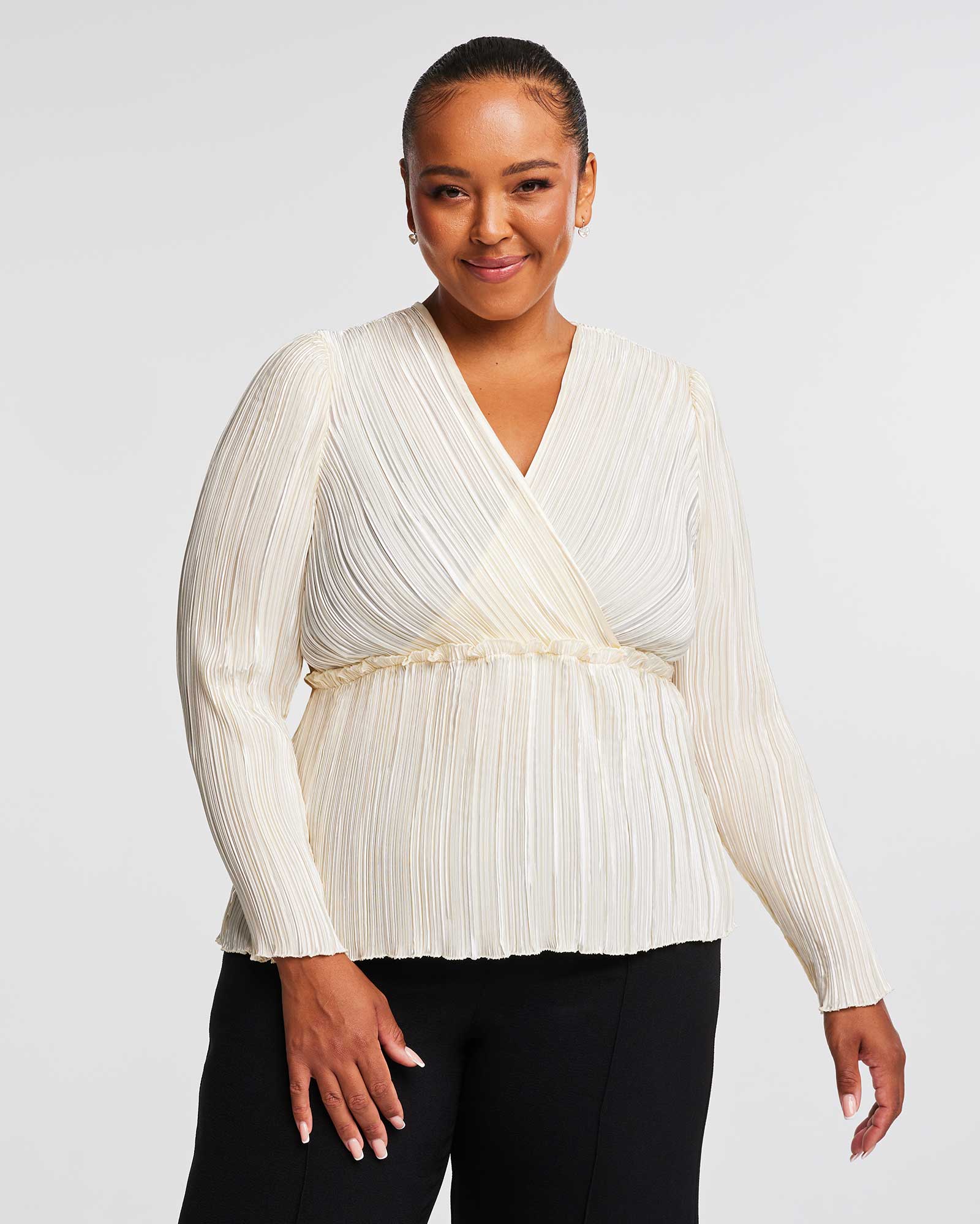 A plus-size woman wearing an Alexandra Cream Wrap-Illusion Pleated Top and black pants.